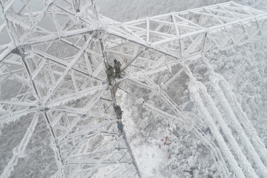 電力應(yīng)急處置人員爬上70米高的±800千伏陜武輸電線路1898號塔，通過機(jī)械震動方式清除地線和光纜上的積雪。鄒小民攝 