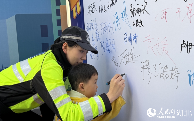 歲的小男孩在交警小姐姐帶領(lǐng)下，在文明禮讓承諾墻簽下自己的大名。人民網(wǎng)記者 周恬攝